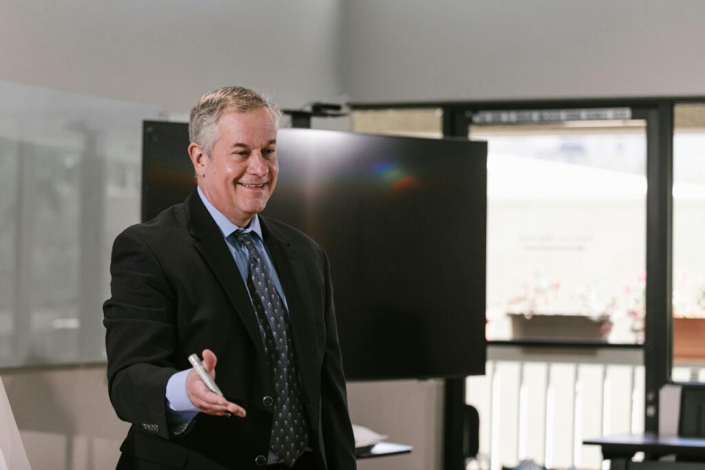 Businessman presenting in a conference room with a smile, holding a marker and engaging the audience.